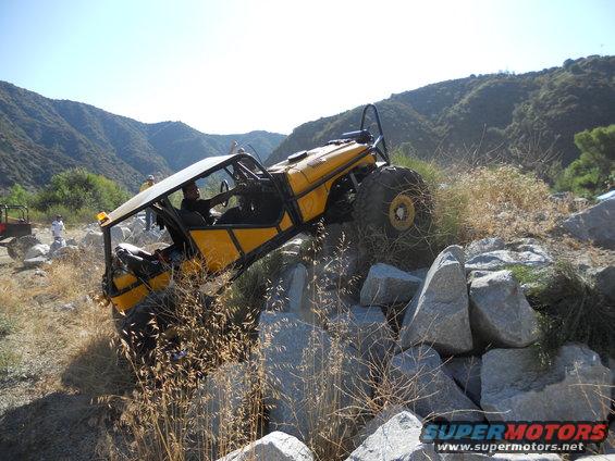 Yellow off-road buggy with roll cage navigating a rocky incline, another off-road vehicle visible in background