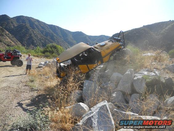 Yellow off-road vehicle tilted on rocks with a red ATV in the background