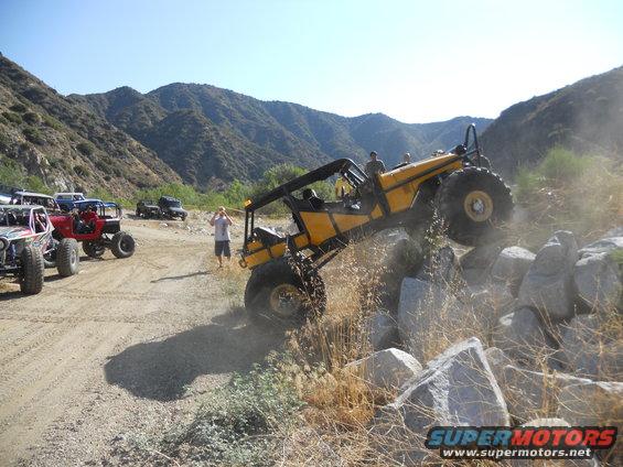 Yellow off-road vehicle climbing rocks, with other off-road vehicles in background