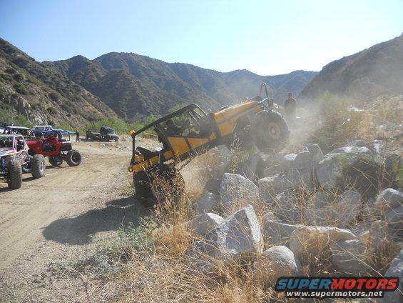 Yellow off-road buggy climbing over rocks with other vehicles in background