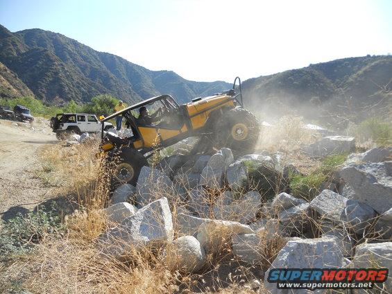 Yellow off-road vehicle climbing rocks, with a white Jeep in the background