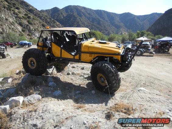 Yellow off-road vehicle with a roll cage and large tires on rocky terrain