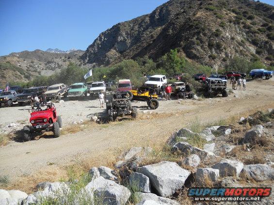 Group of off-road vehicles parked on a dirt road with mountains in the background