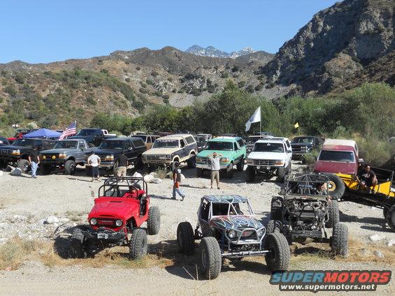 Group of off-road vehicles parked in a dry riverbed with mountains in the background