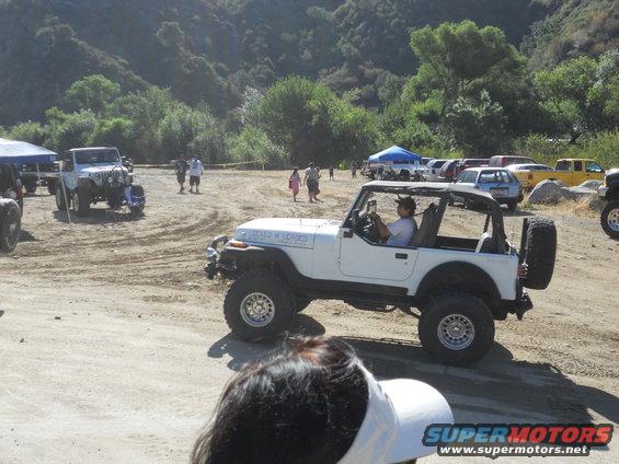White Jeep Wrangler with a roll cage and off-road tires parked on a dirt lot