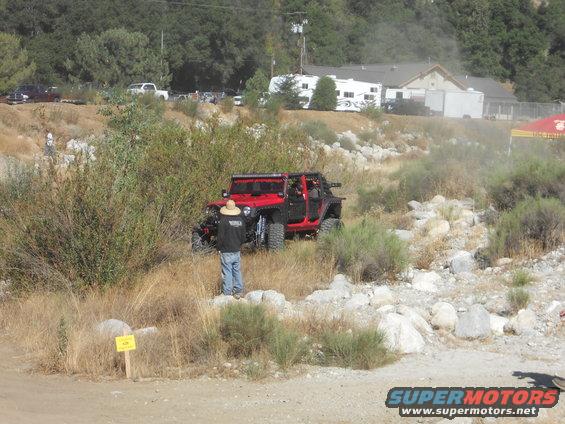 Red off-road Jeep with roll cage driving on a dirt path