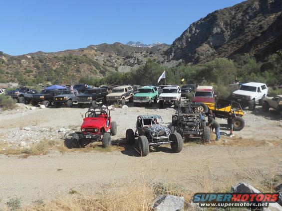 Off-road vehicles parked in a dry, mountainous area. A red Jeep is in the foreground