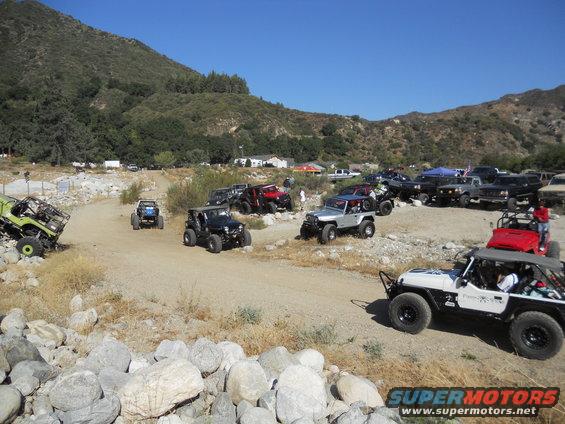 Off-road vehicles gathered on a dirt path with mountains in the background