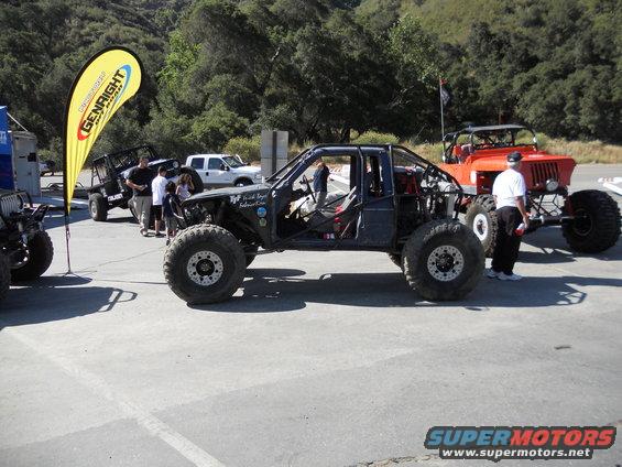 Modified off-road buggy with roll cage, open doors, and large tires. Another off-road vehicle is visible behind it