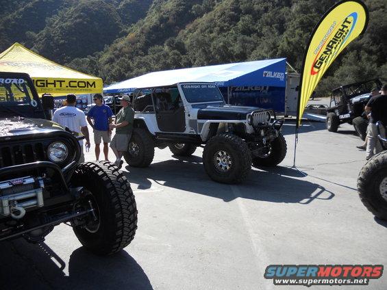 Modified Jeep Wrangler with large tires, parked near tents and a yellow flag. Another Jeep is in the foreground