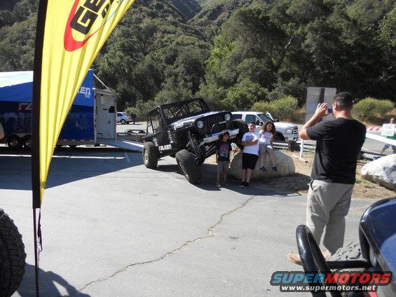 Black off-road vehicle with large tires and roll cage, parked on pavement