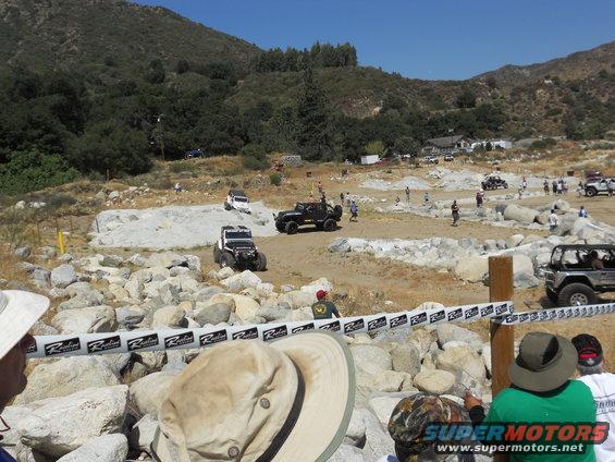 Off-road course with several Jeeps navigating rocky terrain, spectators watching