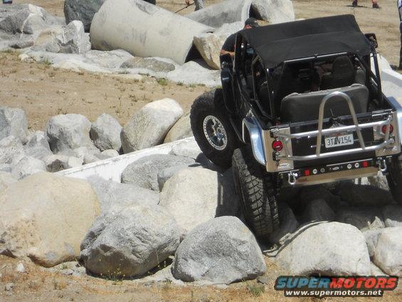 Black off-road vehicle with a soft top, climbing over large rocks. License plate reads 3TV154