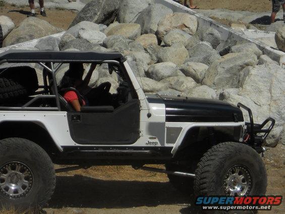 Modified Jeep Wrangler TJ, black and white, with large tires and roll cage, parked on rocky terrain