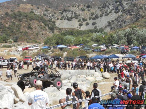 Custom off-road buggy with pink wheels navigating rocks, crowd watching