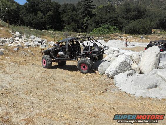 Off-road buggy with roll cage and pink rims navigating rocky terrain