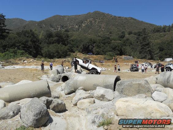 White off-road vehicle with a roll cage climbing over concrete pipes and rocks