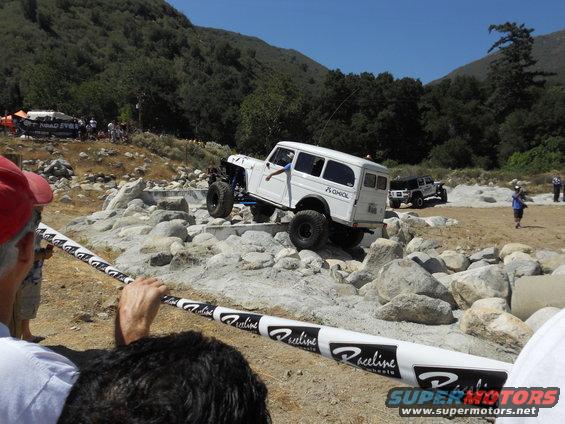 White off-road wagon climbing over rocks, another jeep in background