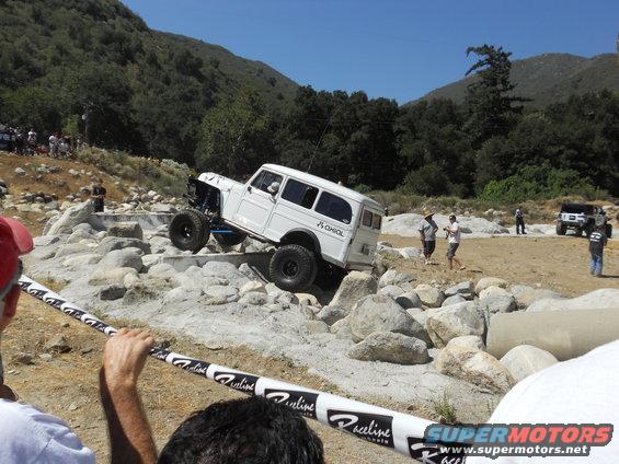 White off-road wagon with large tires navigating a rocky obstacle course