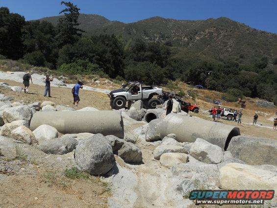 Off-road vehicles on rocky terrain with concrete pipes, people watching