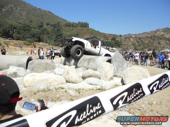 White off-road truck navigating concrete pipes, with spectators watching
