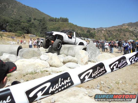 White off-road truck with large tires navigating a rocky obstacle course