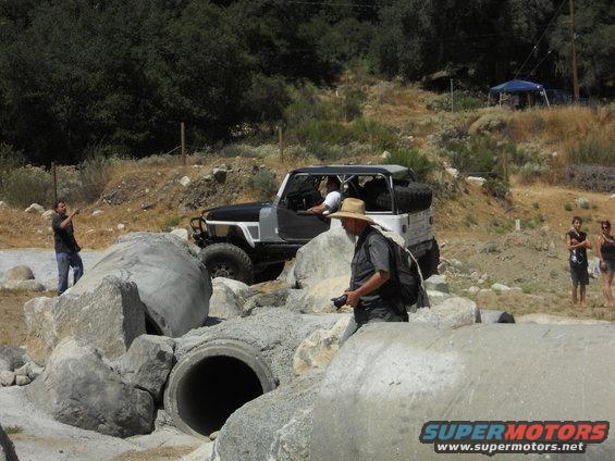 Black and white Jeep Wrangler with spare tire on rear, navigating rocky terrain