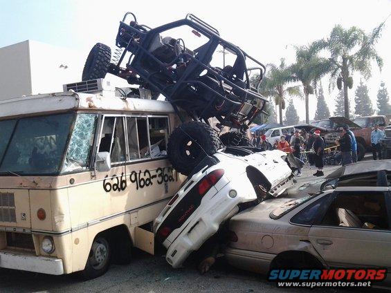 Dune buggy atop crushed cars and RV with phone number 626-962-3621 visible