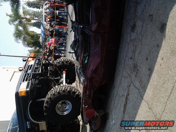 Modified truck with large tires next to a crushed red car