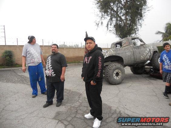 Mud-splattered pickup truck with oversized tires, lifted suspension, and a flag on top