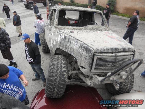 Mud-caked pickup truck with big tires, people around it