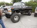 1986 Ford Bronco - This lifted black Ford pickup truck, likely from the late 1970s, is parked outdoors next to another vehicle.
