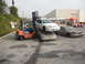 1986 Ford Bronco - A forklift stacks a white car on top of a tan Ford Taurus, with another car to the right.