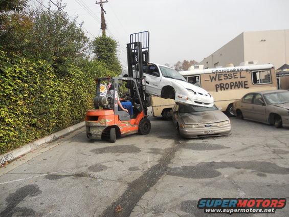 Forklift stacking a white car on top of a tan car, with a Wessel Propane truck behind