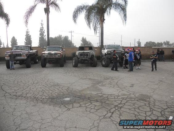 Four lifted trucks parked in a lot, one with a person standing next to it
