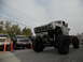 1986 Ford Bronco - A heavily modified white Ford truck with oversized tires is parked alongside other vehicles.