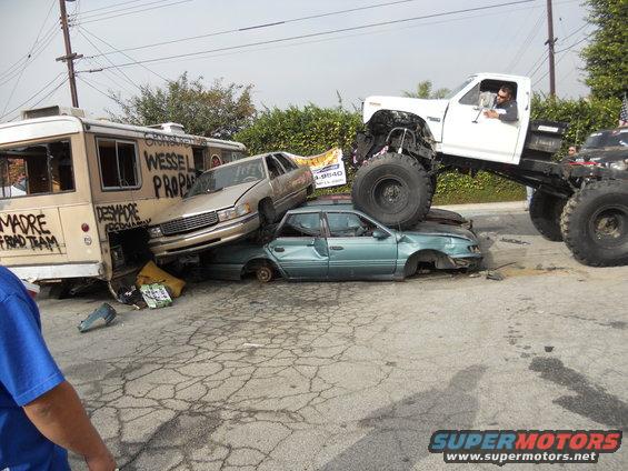 Monster truck on top of crushed cars, with a bus on the side