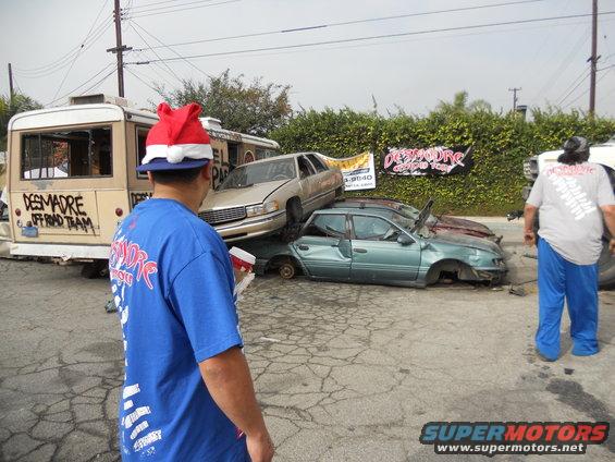 Pile of wrecked cars, one with a Santa hat on a person nearby