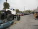 1986 Ford Bronco - Monster truck dominates the scene, crushing a sedan while other trucks line the street.