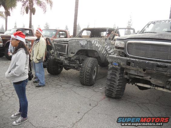 Several heavily modified trucks with large tires and some people wearing Santa hats