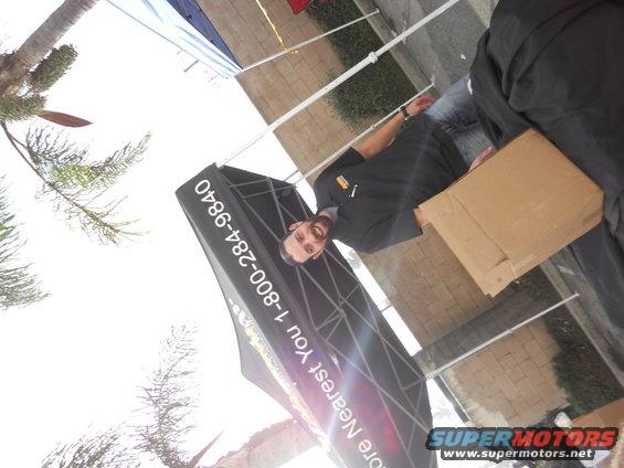 Man stands by a black tent with white text and a Supermotors logo