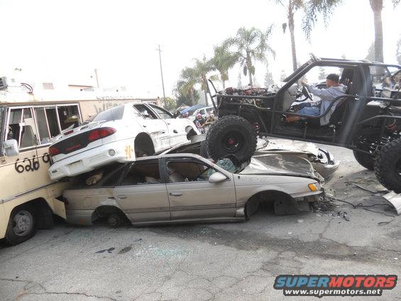 Buggy on top of a pile of wrecked cars, including a white sedan and a tan sedan
