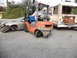 1986 Ford Bronco - Forklift moves a wrecked car near a bus with visible text. The car's front end is heavily damaged.