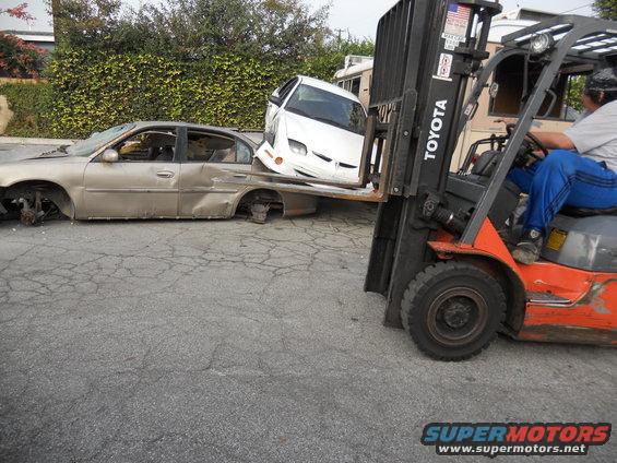 Forklift moving a wrecked gold sedan and a white car