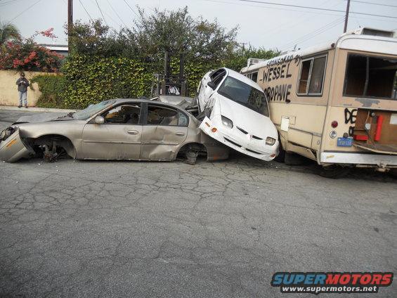 Damaged gold sedan and white car crushed against a propane truck