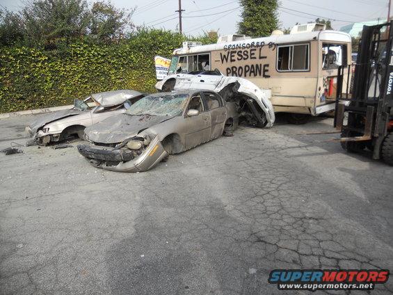 Two heavily damaged sedans are in front of a truck labeled "WESSEL PROPANE"; a forklift is to the right