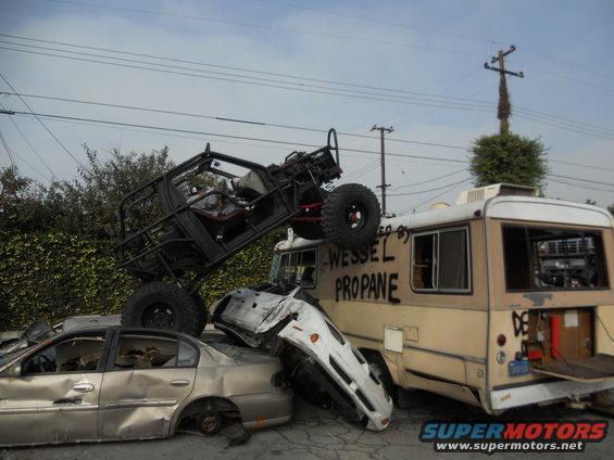 Off-road vehicle atop a crushed sedan and RV, with 'WESSEL PROPANE' spray-painted on the RV