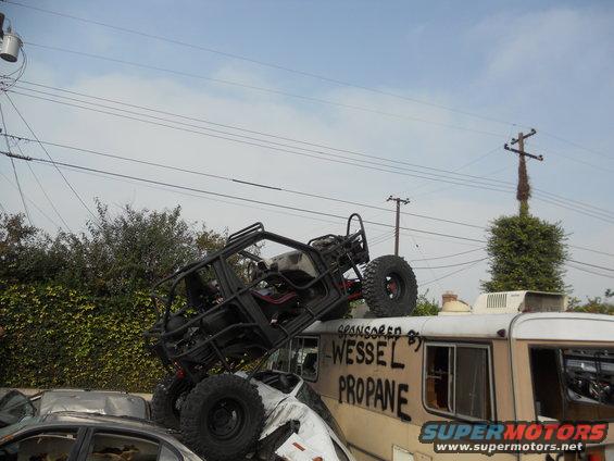 Black off-road buggy on top of a white car, which is on a camper van. Wessel Propane text visible