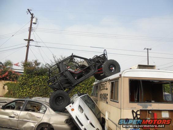 Off-road buggy perched on an RV, which is on top of other wrecked cars. Text on RV reads 'Vessel Propane'
