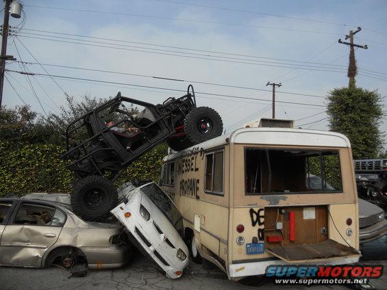 Off-road buggy on top of a wrecked bus, which is on top of other cars. Text on bus says 'WESSEL PROPANE'
